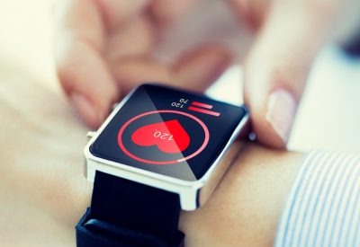 technology, health care and people concept - close up of woman hands checking pulse by smartwatch with heart icon on screen